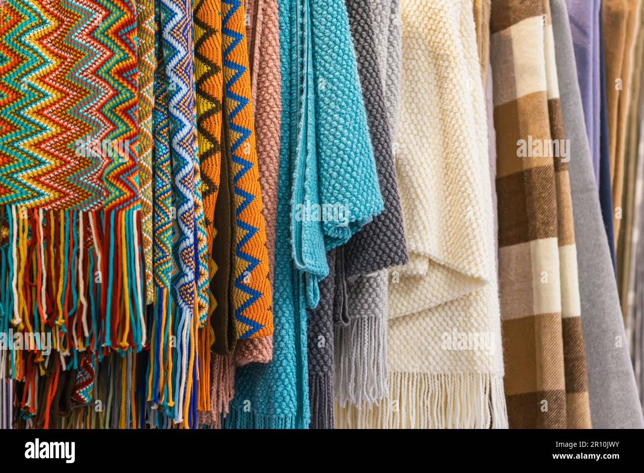 Close-up of multi-colored plaids, stoles hanging in row in store, cozy seasonal goods. Autumn winter shopping concept Stock Photo