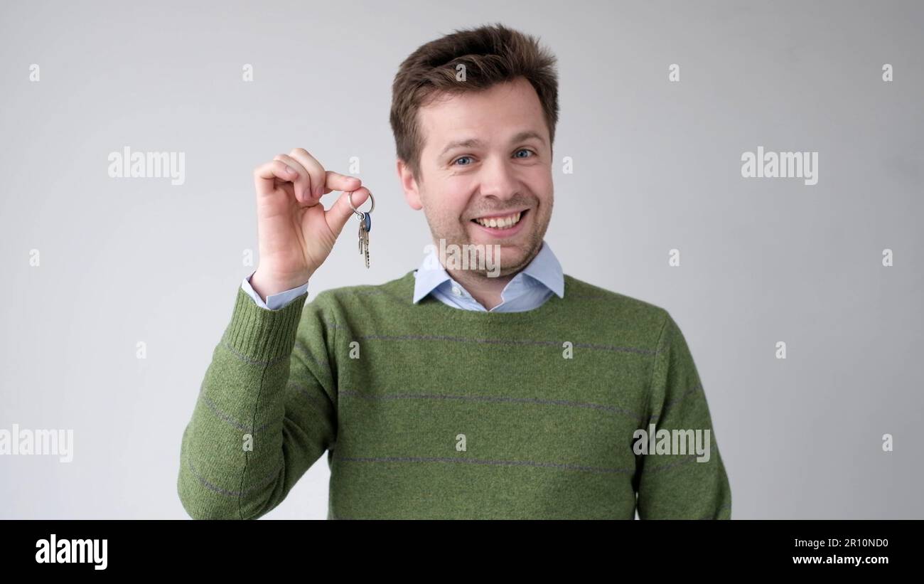 A European young man shows the keys to his new apartment. He is happy ...