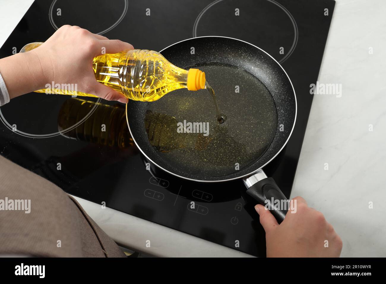 Woman pouring cooking oil from bottle into frying pan on stove, above view Stock Photo