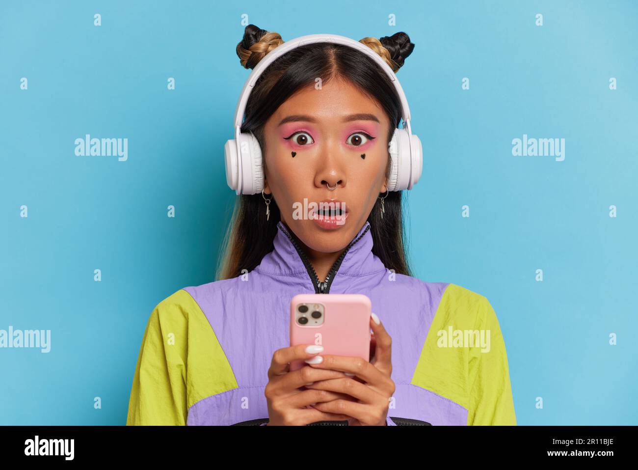 Surprised Vietnamese girl with headphones poses on blue studio