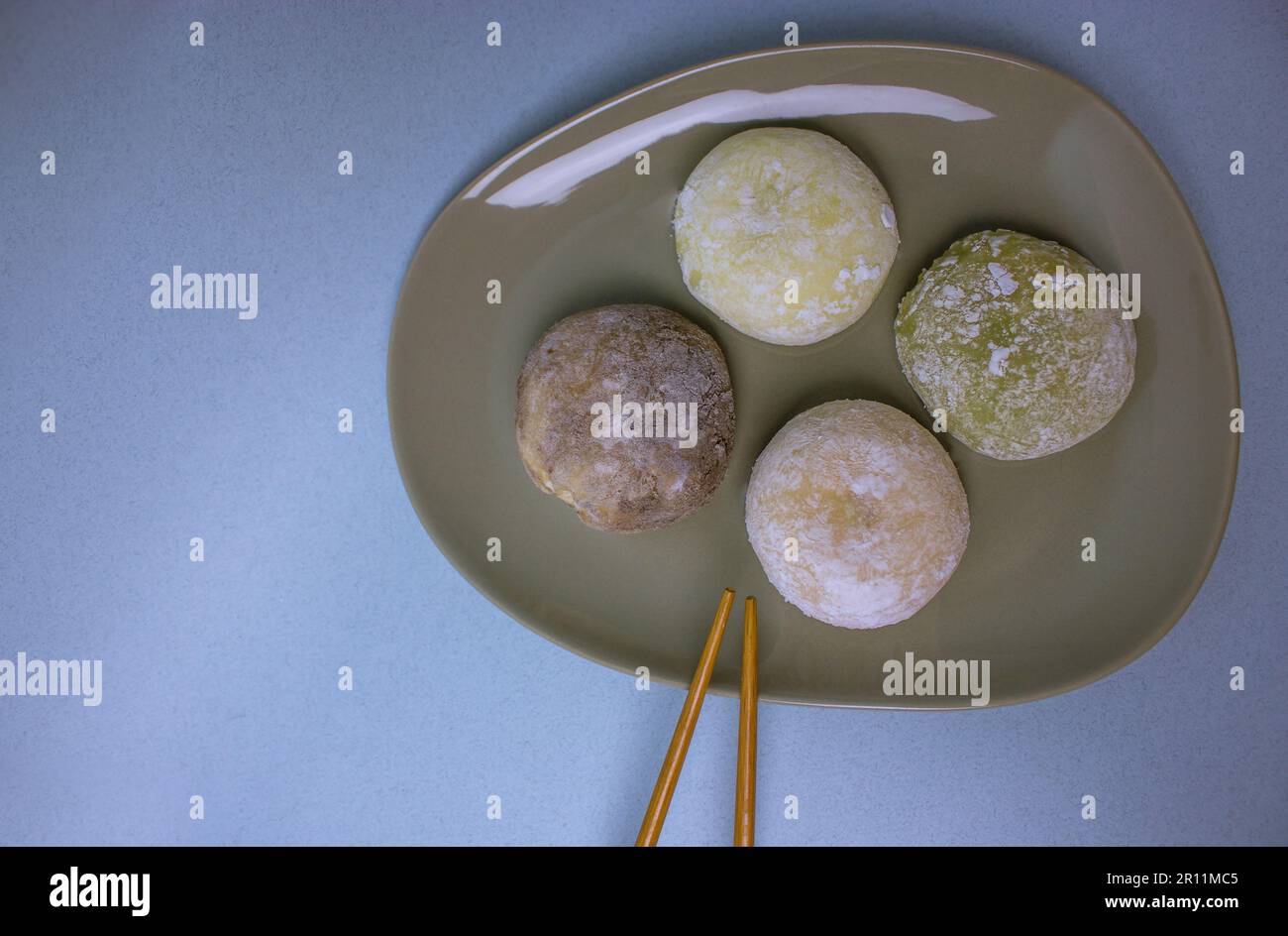 Chopsticks and traditional Japanese dessert mochi or daifuku in rice dough close-up. Four mochi ice cream balls on gray plate on blue-violet table sel Stock Photo