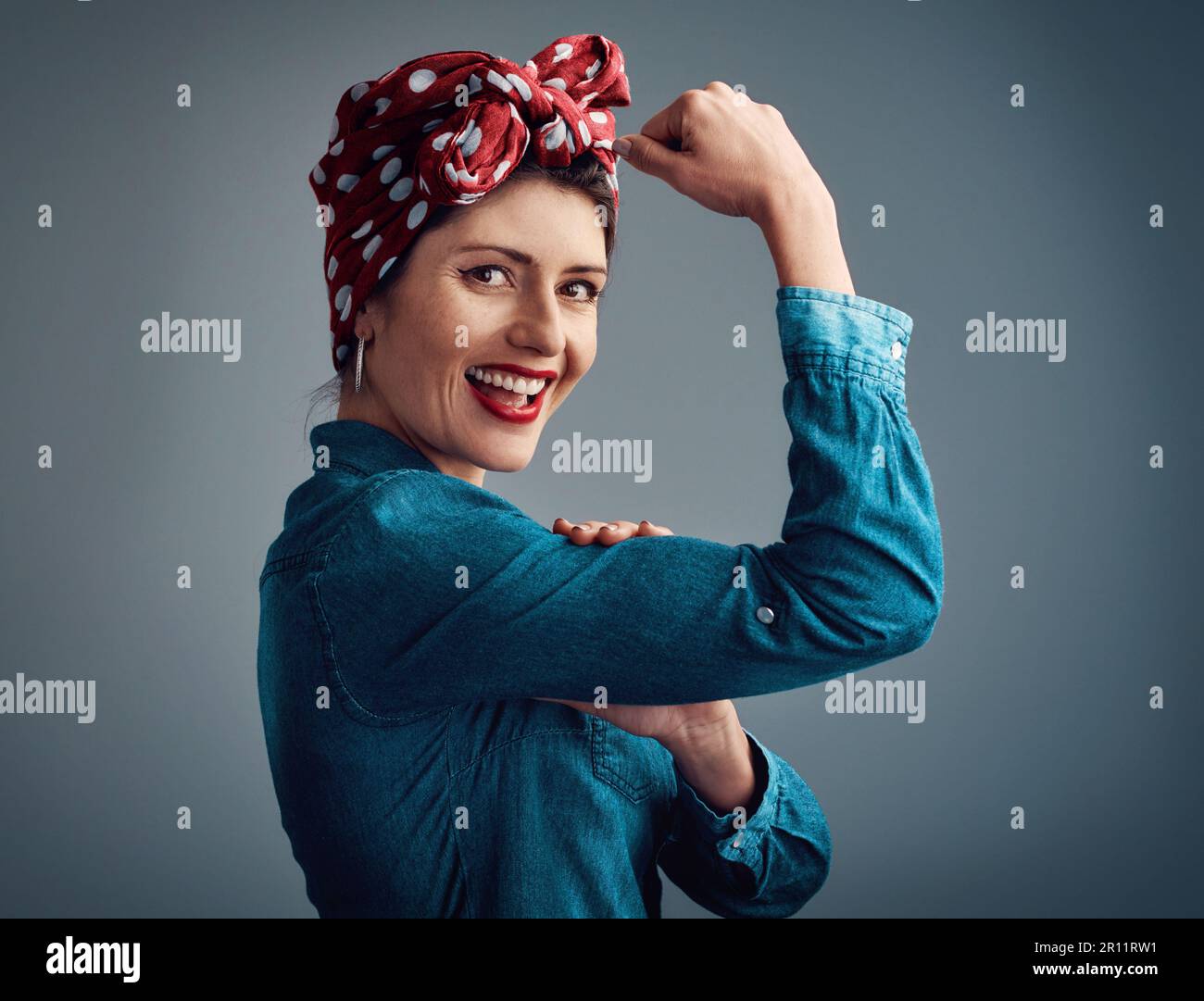 Pinup girl, strong and flexing muscle portrait in studio for beauty, women power and fashion. Happy female person show bicep on a grey background for Stock Photo