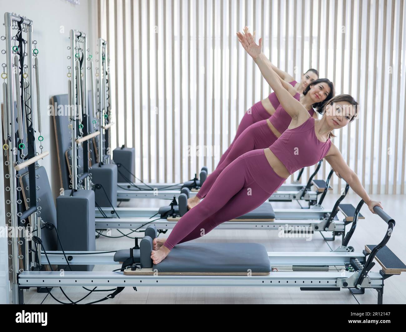 Three Asian women in pink sportswear doing side planks on a reformer