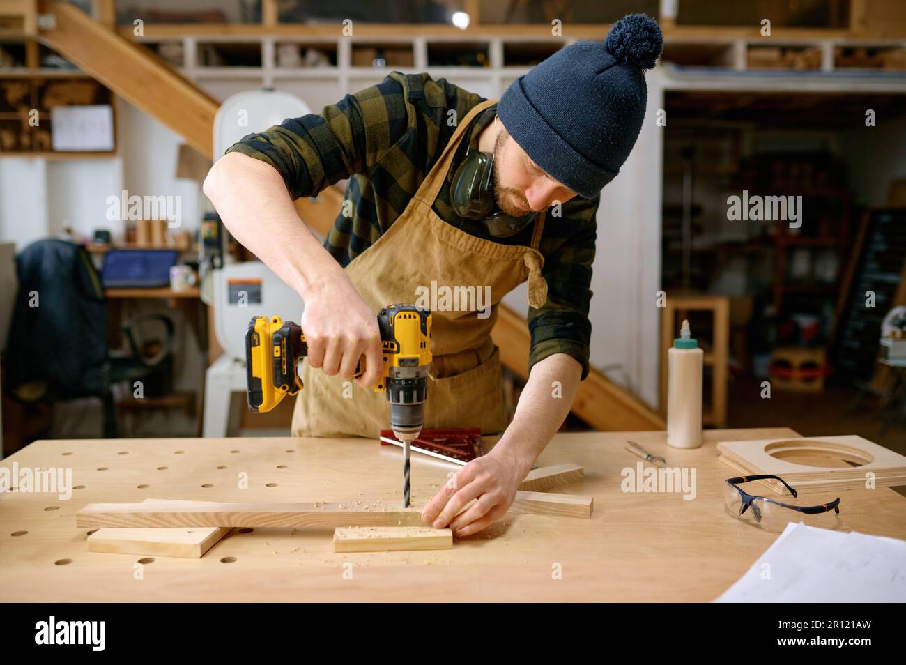 Young man jointer working with drill leaning over table at carpentry workshop Stock Photo