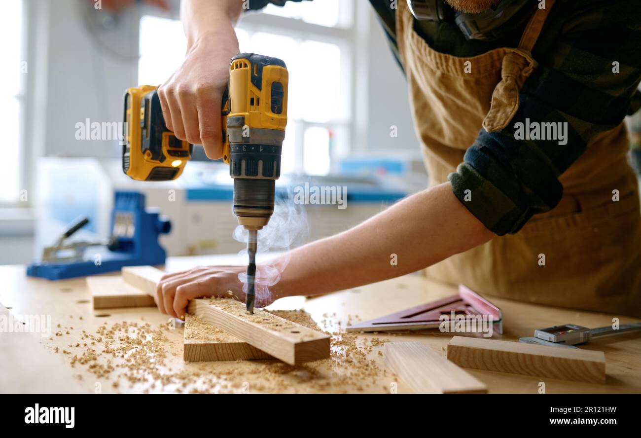 Carpenter working with drill leaning over table at carpentry workshop Stock Photo