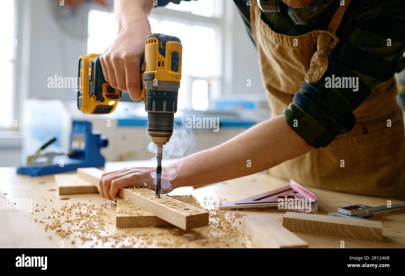 Carpenter working with drill leaning over table at carpentry workshop Stock Photo