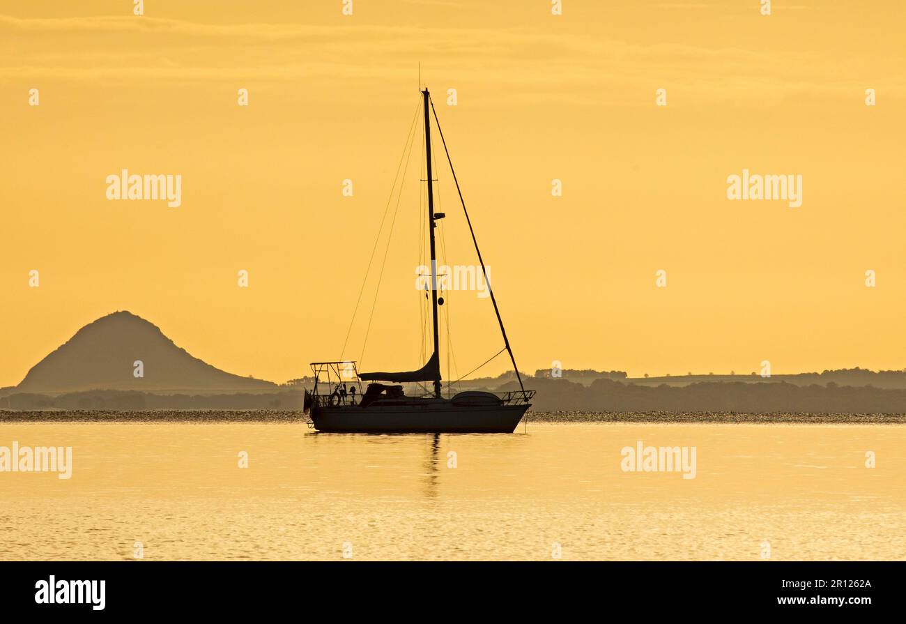 Portobello, Edinburgh, Scotland, UK. 11 May 2023. Sun slow to appear over the bank of cloud on the horizon at the Firth of Forth. Temperature 7 degrees but felt pleasantly mild with little or no breeze. Pictured: small pleasure sailing yacht berthed in Firth of Forth with Berwick Law in the background. Credit: Arch White/alamy live news. Stock Photo