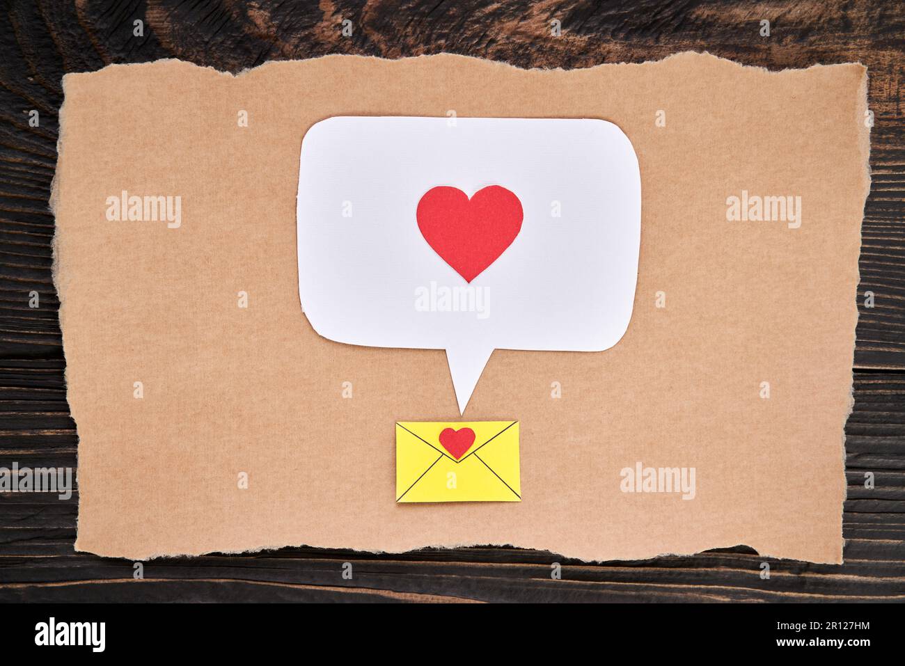 Postcard with email icon, red heart and speech bubble in paper art style. Love letter, greeting card, invitation mockup over dark wooden background. F Stock Photo
