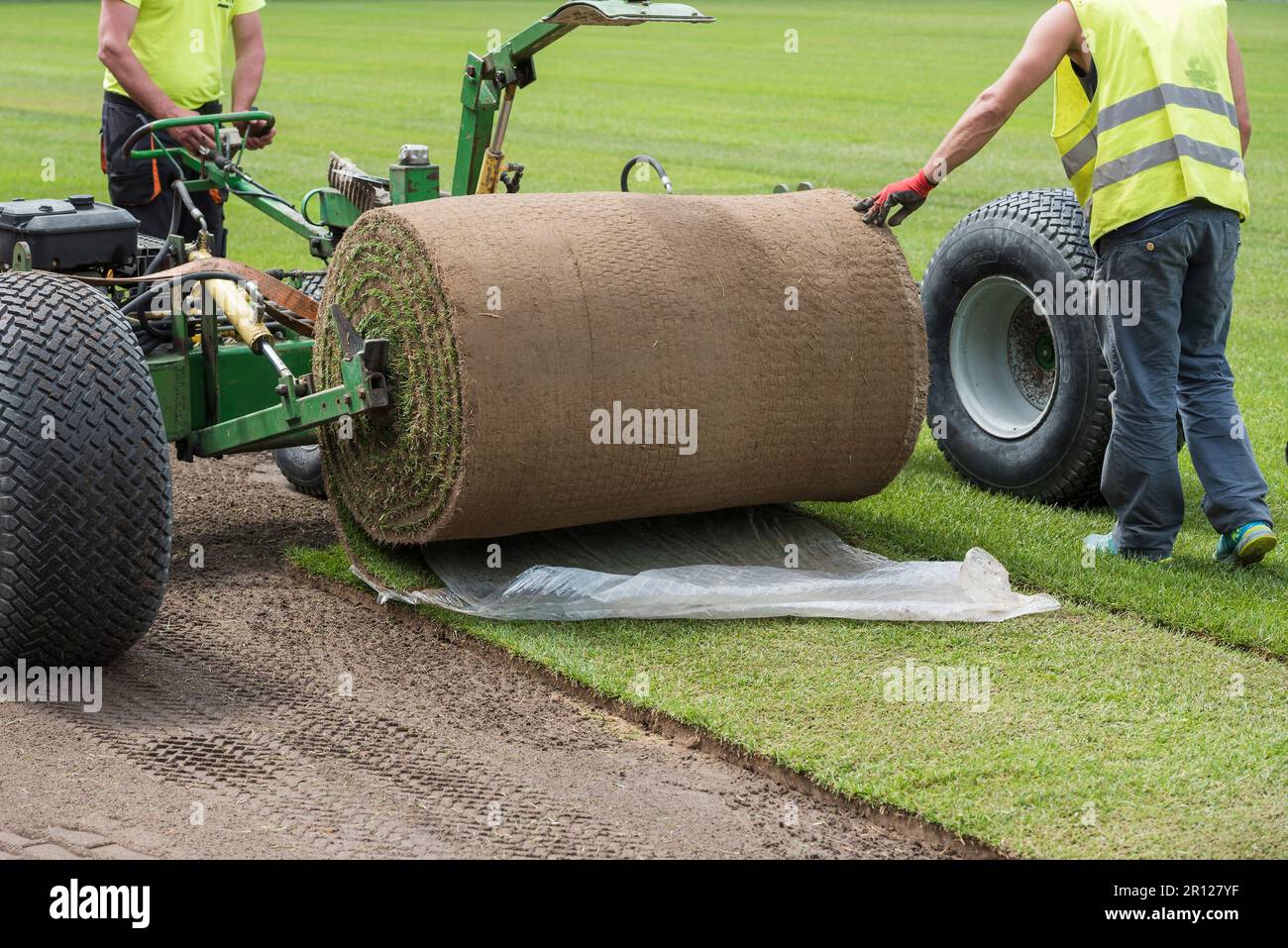 Workers laying grass in a roll on a football field at the stadium Stock