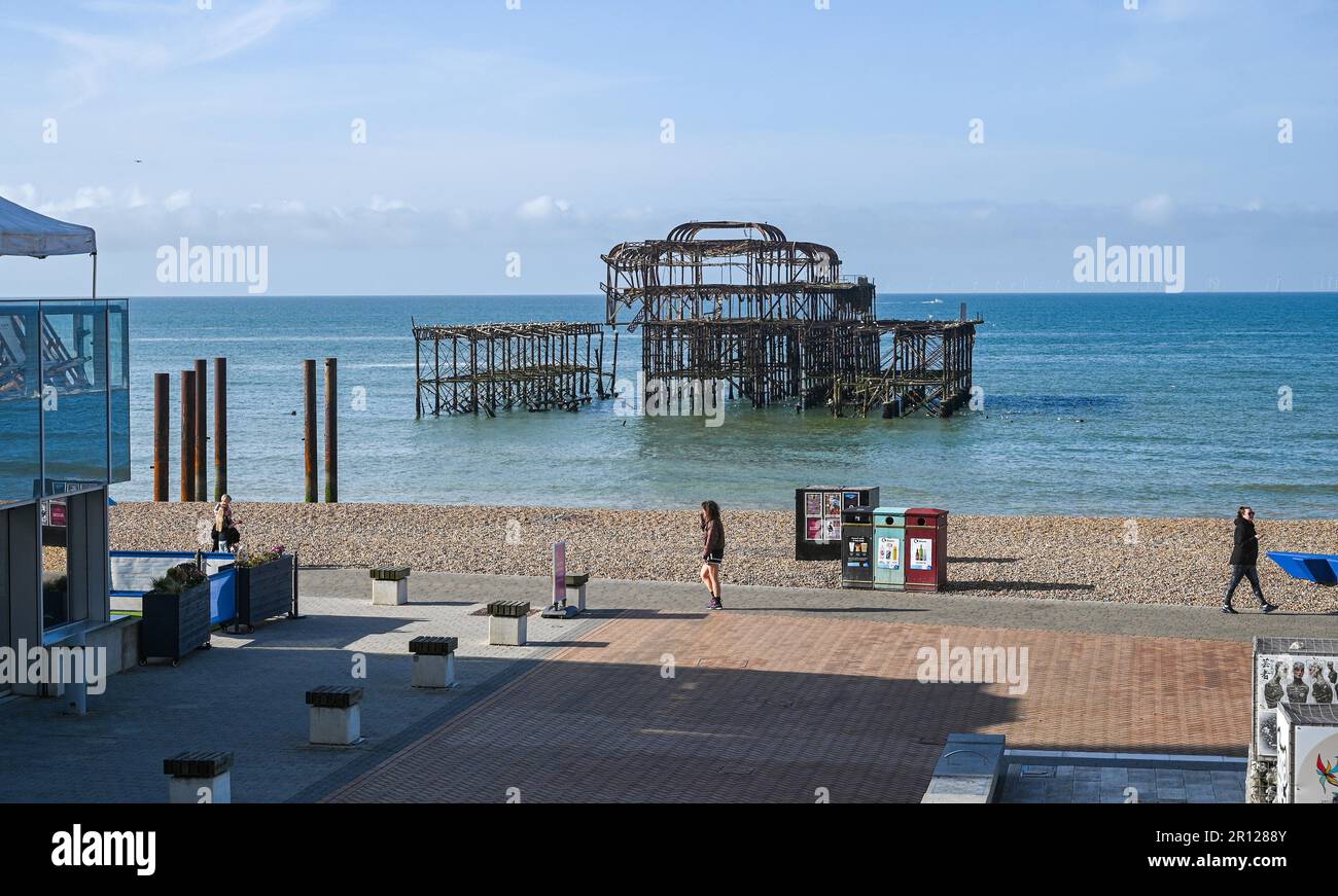 Brighton UK 11th May 2023 - walkers pass by Brighton's West Pier in the early morning sunshine along the South Coast : Credit Simon Dack / Alamy Live News Stock Photo