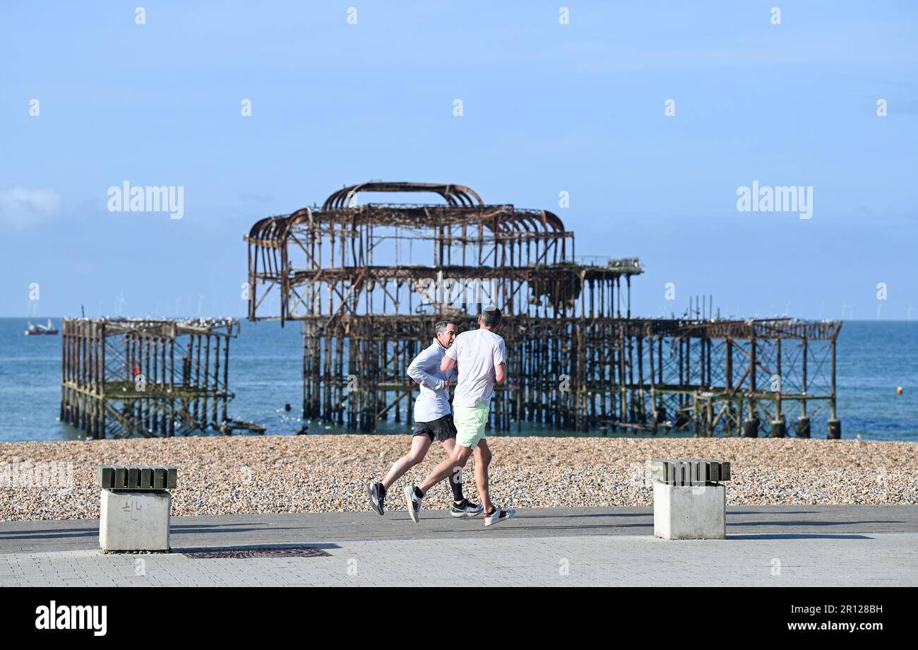 Brighton UK 11th May 2023 - Runners pass by Brighton's West Pier in the early morning sunshine along the South Coast : Credit Simon Dack / Alamy Live News Stock Photo