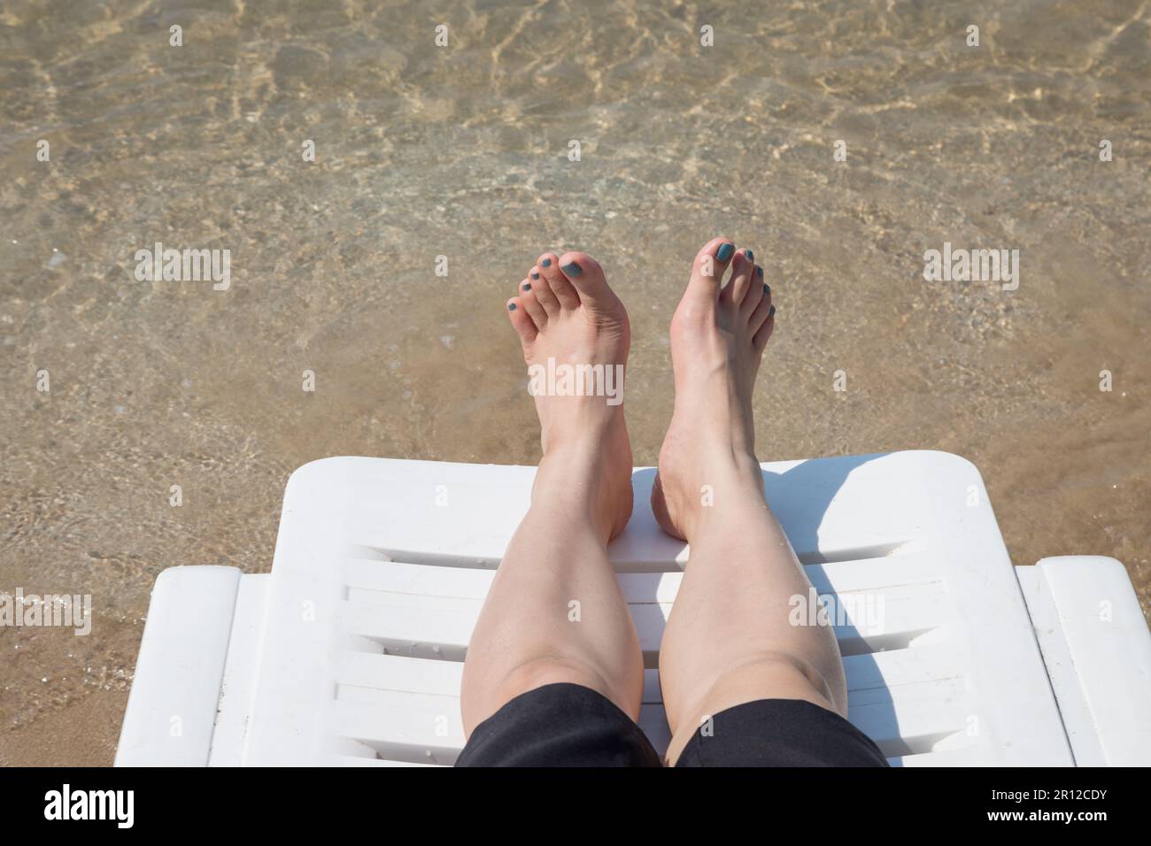 Vacation on tropical beach Woman's legs on the beach bed with clear ocean water background Stock Photo