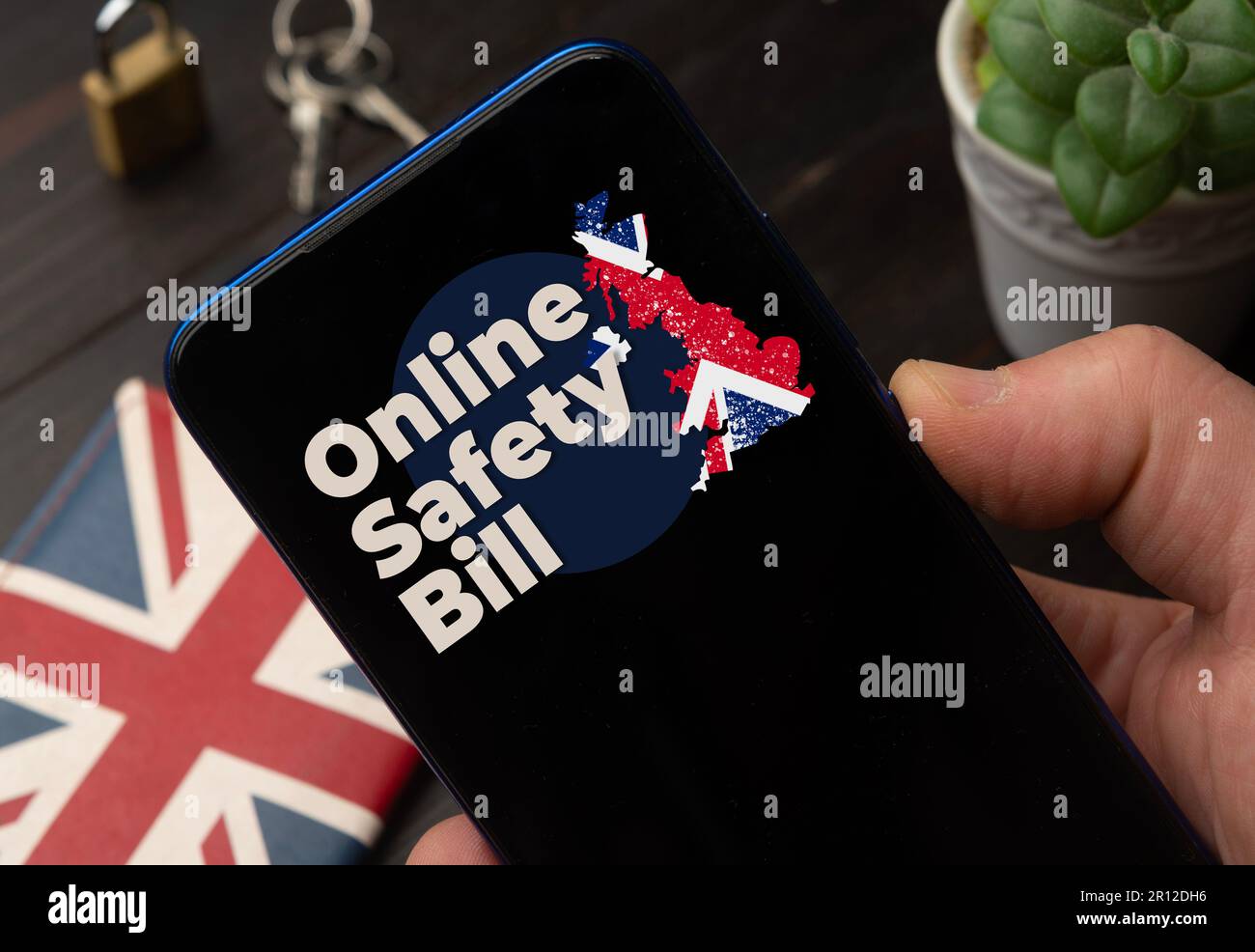 Online Safety Bill (OSB) UK concept: man hold a smartphone over a wooden desktop Stock Photo