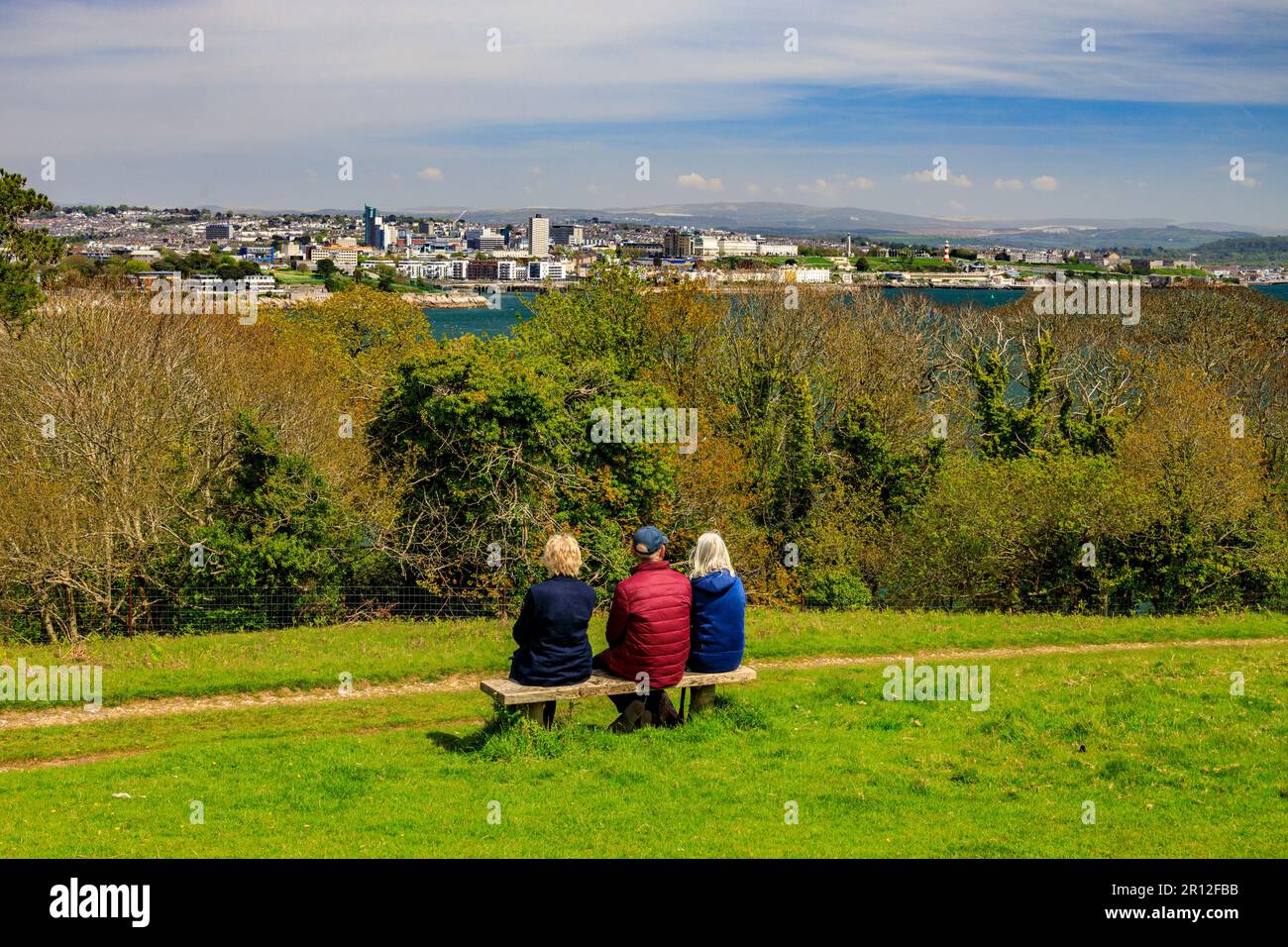 Three visitors looking across the River Tamar towards the Plymouth waterfront and The Hoe from Mount Edgcumbe Country Park, Cornwall, England, UK Stock Photo