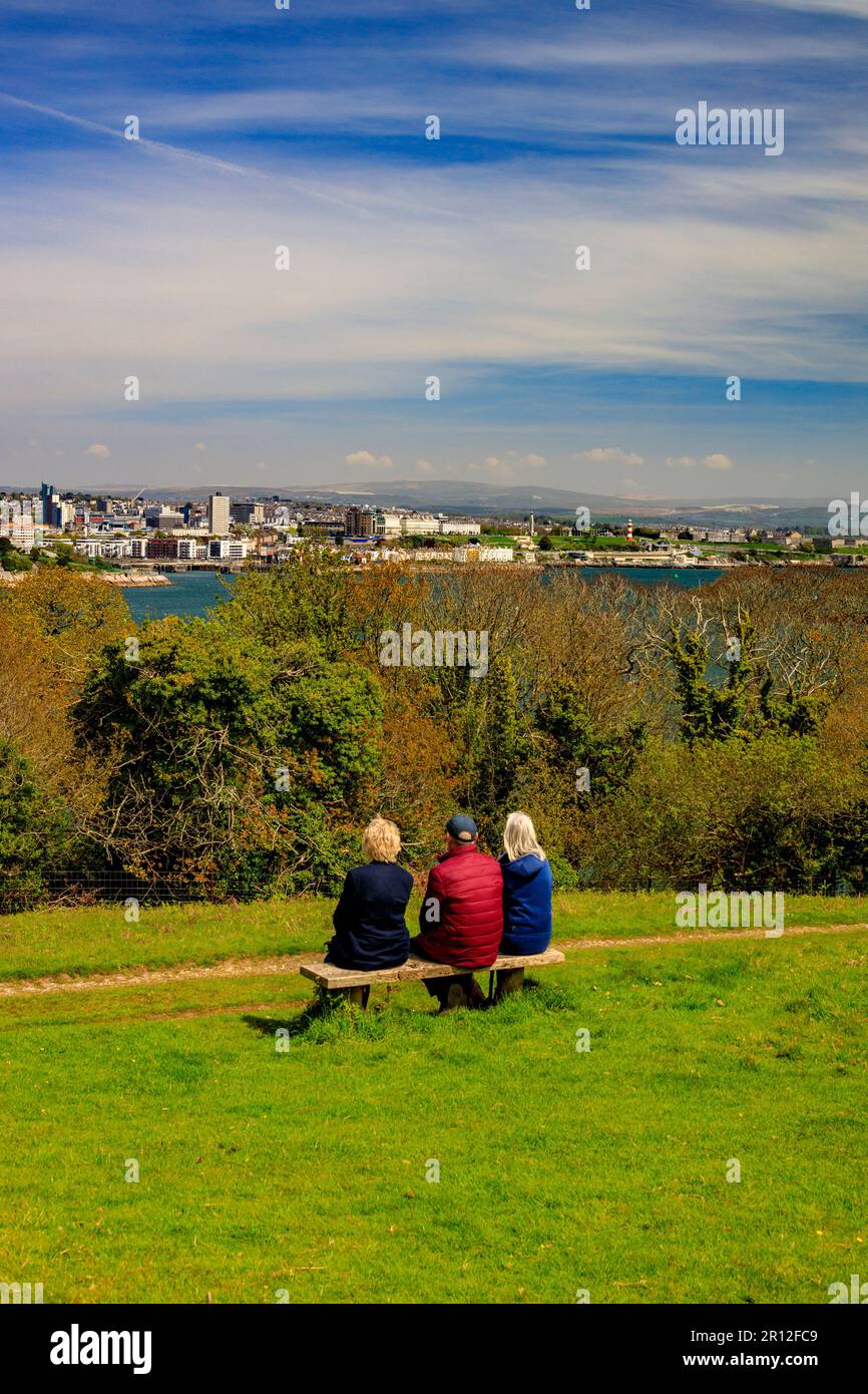 Three visitors looking across the River Tamar towards the Plymouth waterfront and The Hoe from Mount Edgcumbe Country Park, Cornwall, England, UK Stock Photo