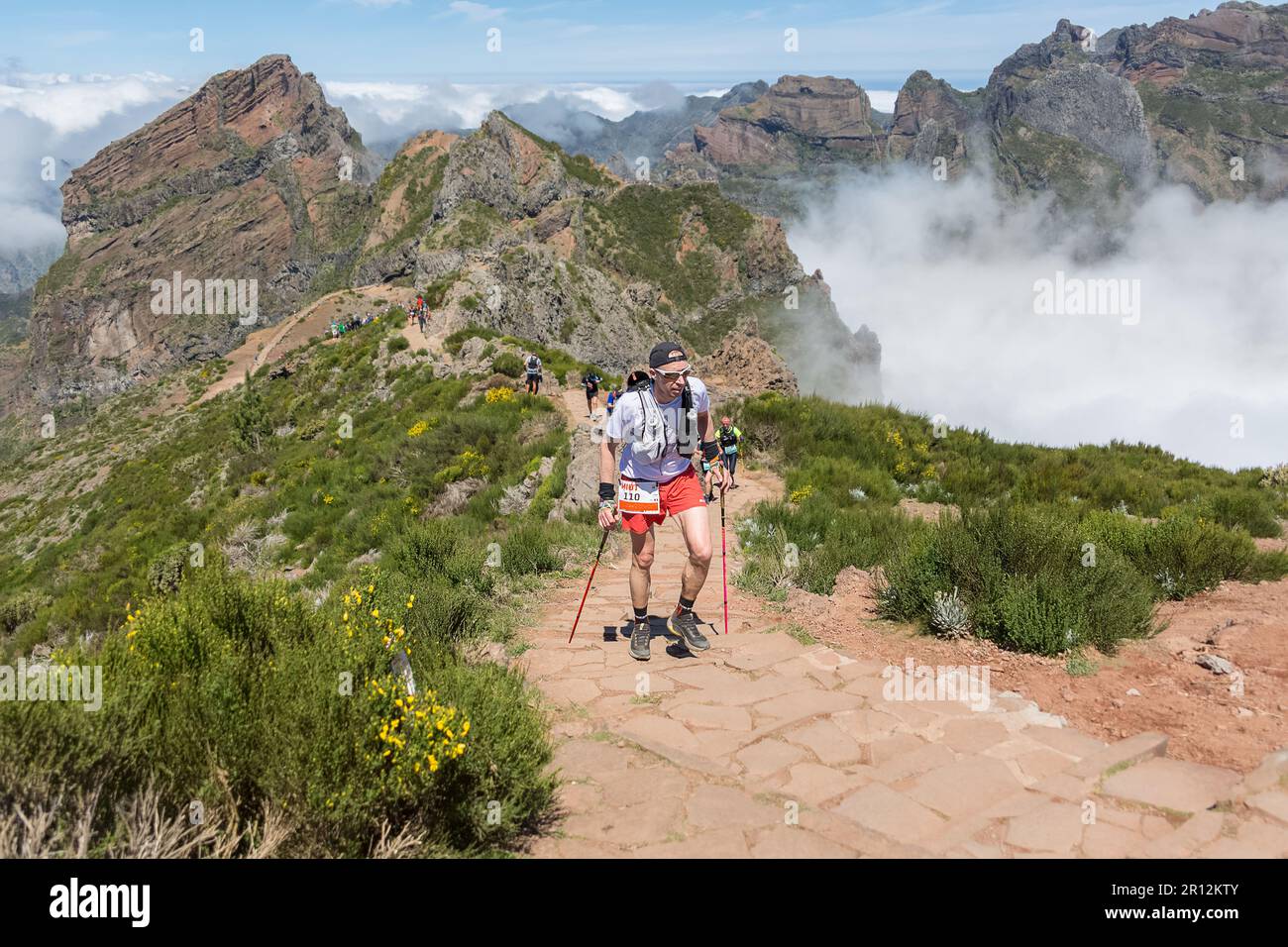 Madeira Island Portugal - 04 22 2023: Rigorously equipped athlete finishing the Pico do Areeiro trail race, low clouds and mountains as background, Ma Stock Photo