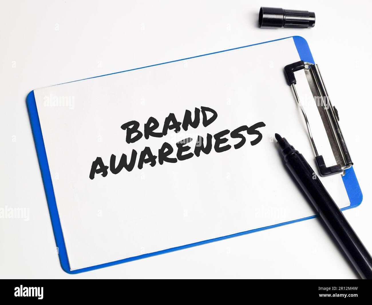 A clipboard with a pen, ink and highlighters displayed against a solid background with the words 'brand awareness' written in black ink Stock Photo