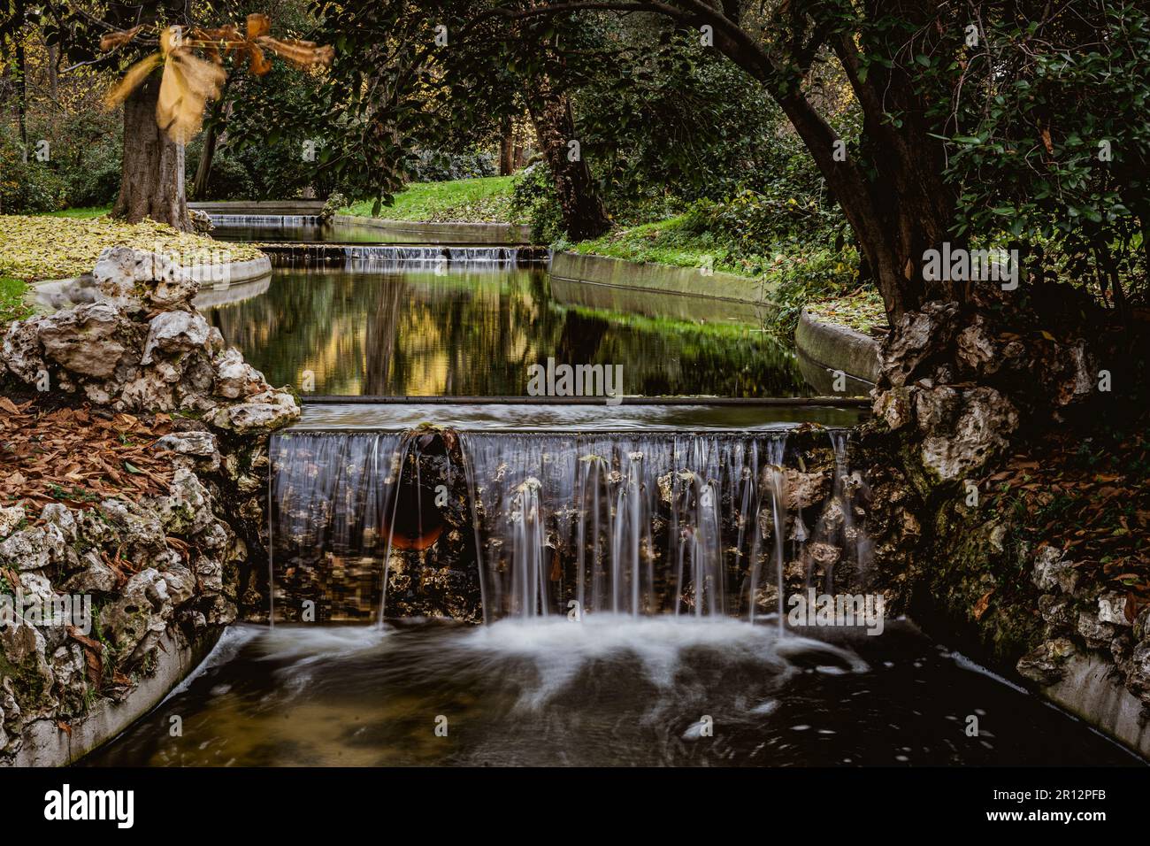 Shallow Waterfall And Rocks A tranquil scene in a public park featuring a small waterfall cascading ...