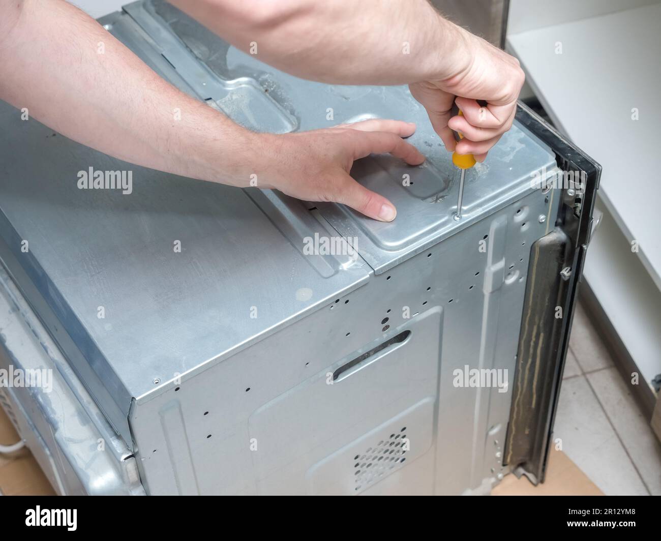 Serviceman unscewing top cover of broken electric oven for easy repair access Stock Photo
