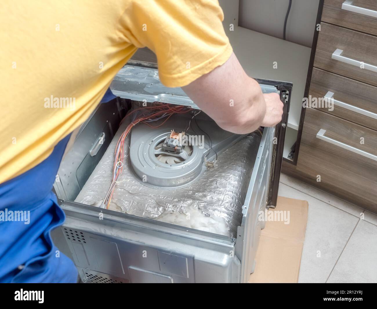Serviceman detaching top cover of broken electric oven for easy repair access Stock Photo