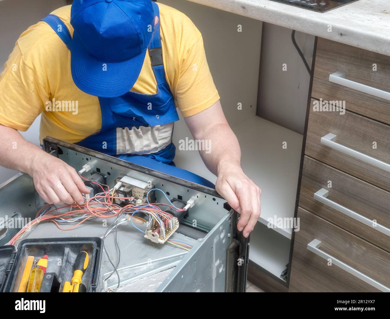 Serviceman replacing faulty part in the broken electric oven Stock Photo