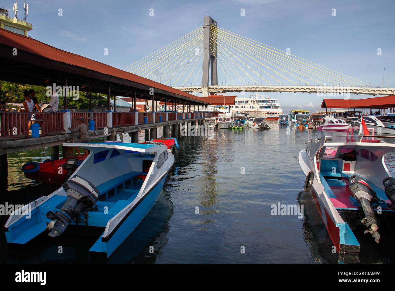 Fishing boats in the harbor with a magnificent bridge in the background, sea water and blue sky. Stock Photo