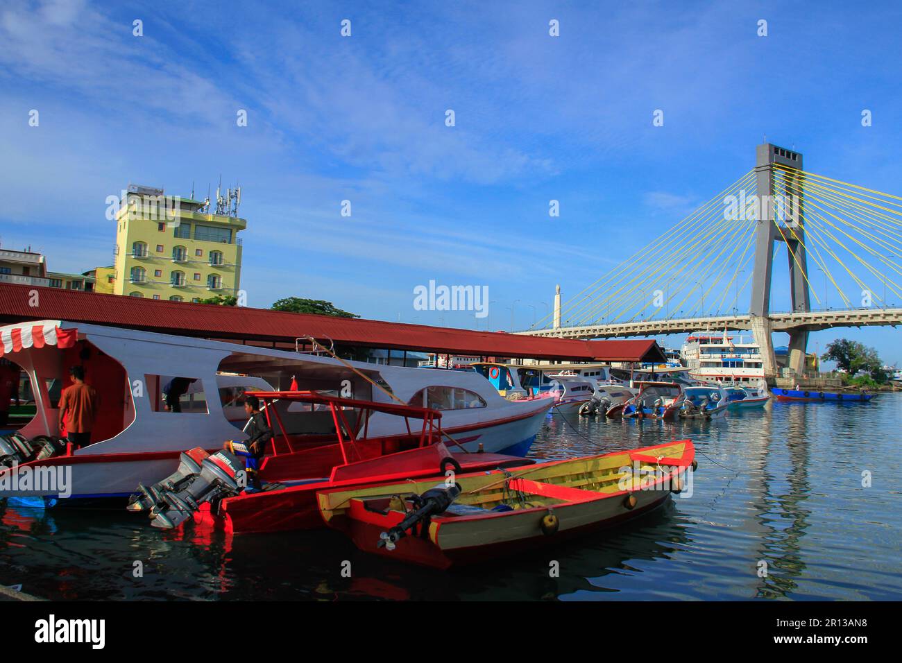 Fishing boats in the harbor with a magnificent bridge in the background, sea water and blue sky. Stock Photo