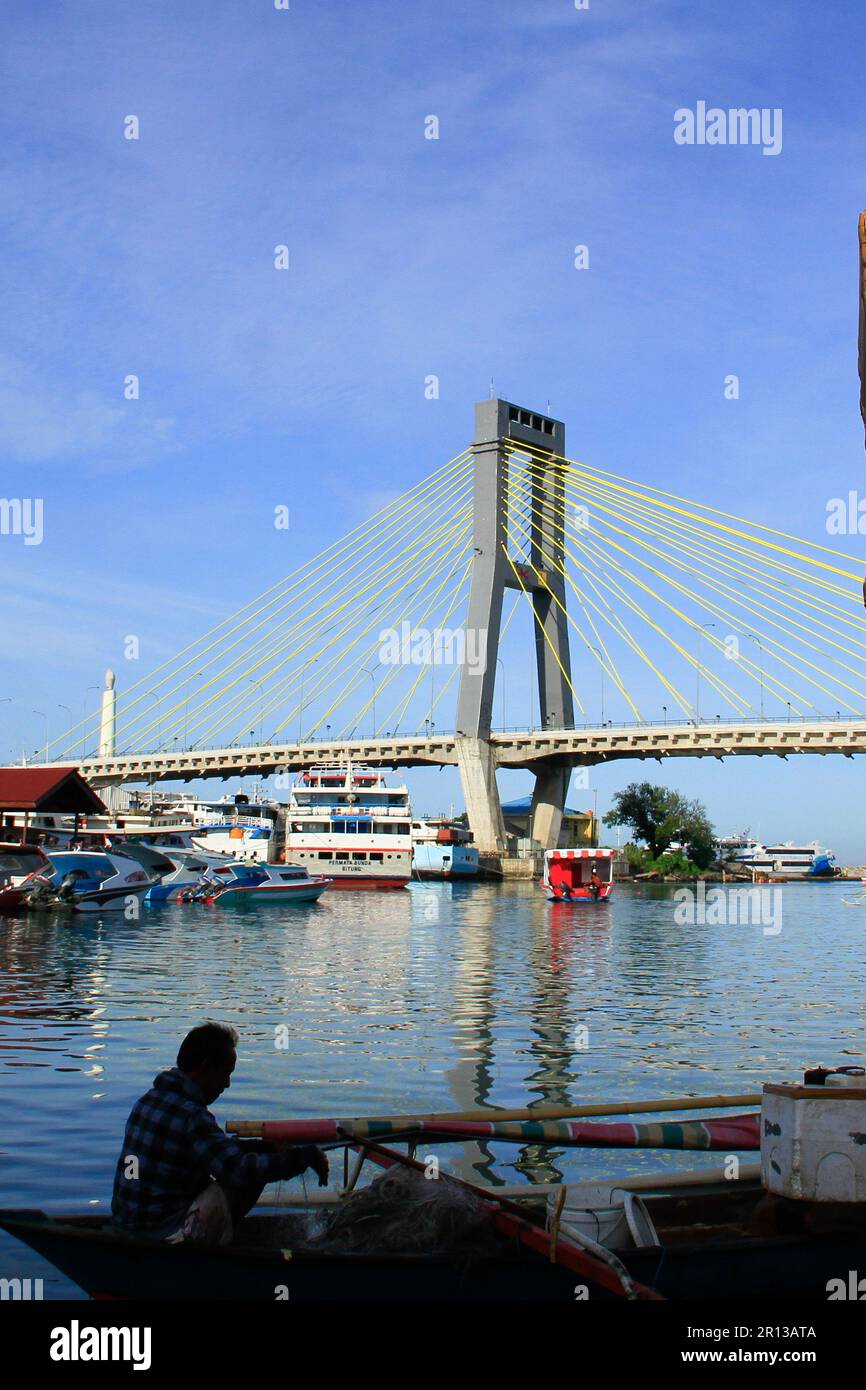 Fishing boats in the harbor with a magnificent bridge in the background, sea water and blue sky. Stock Photo