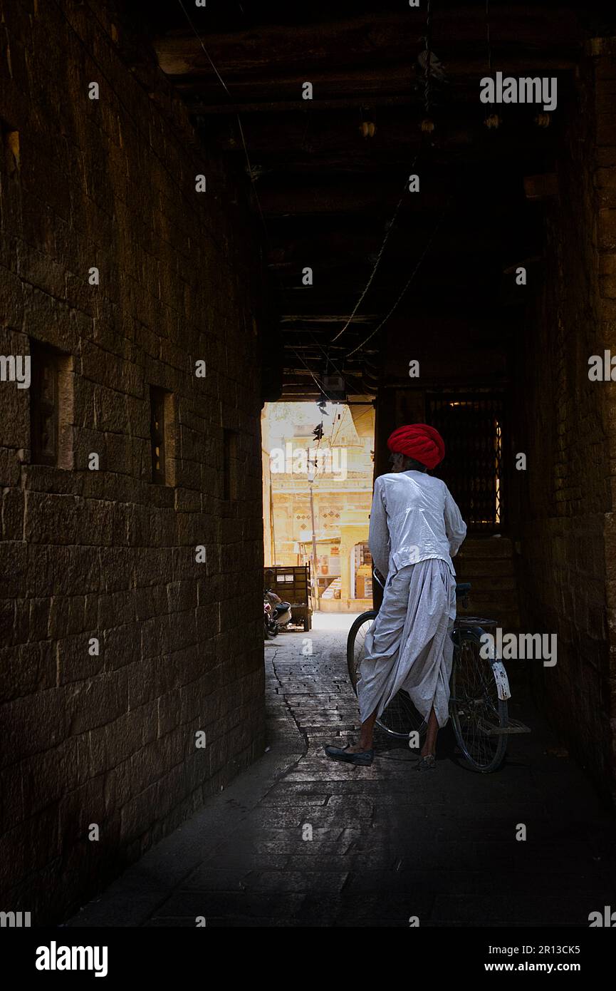 Indian man in traditional clothes walking with its bicycle through a dark passage Stock Photo