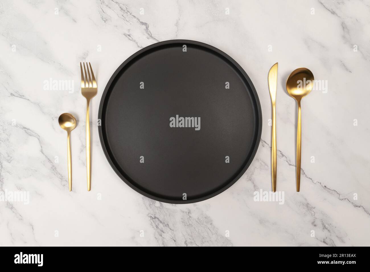 Top view of black plate and gold cutlery on white marble background ...
