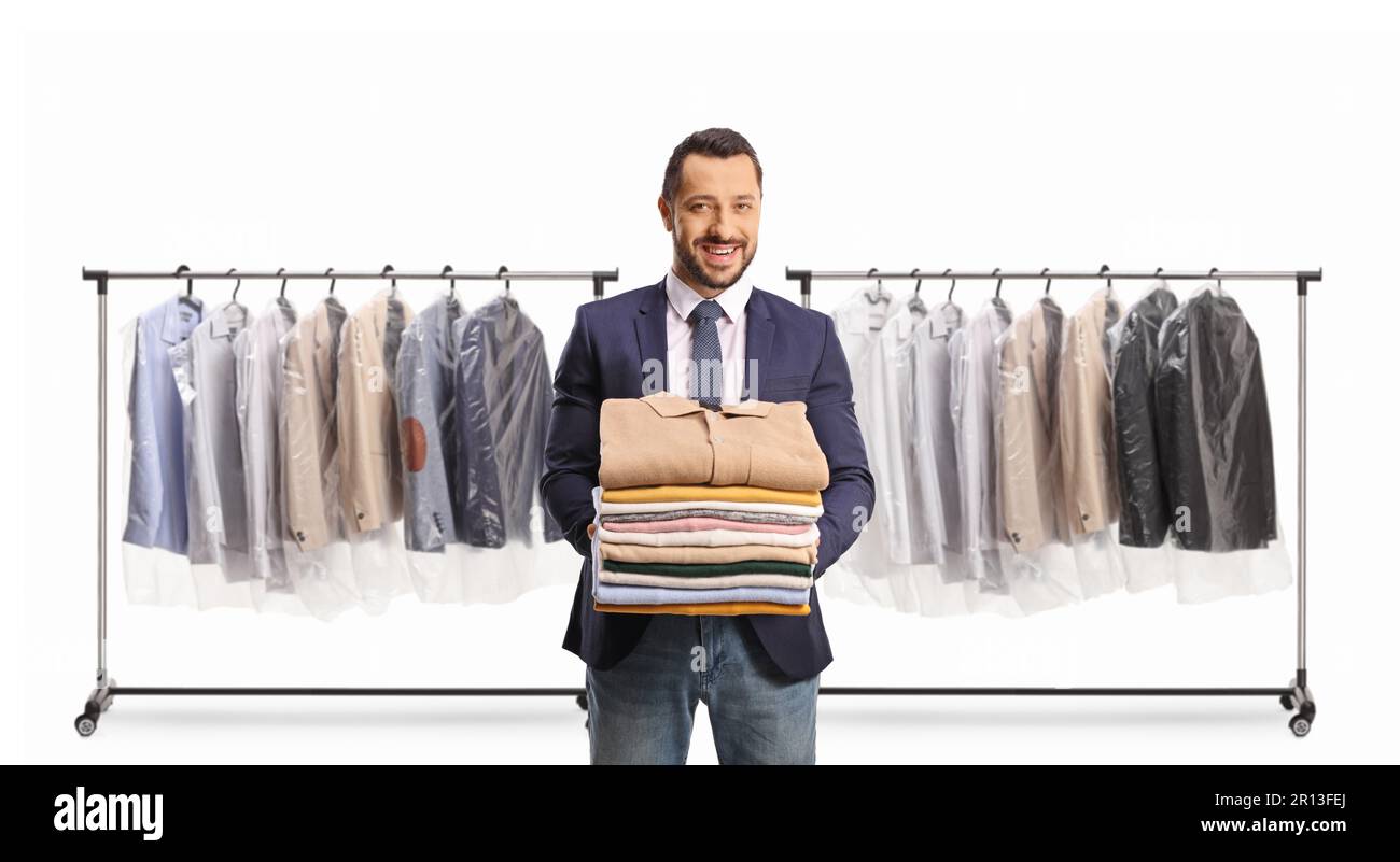 Male customer at dry cleaners holding a pile of folded clothes in front of clothing racks isolated on a white background Stock Photo