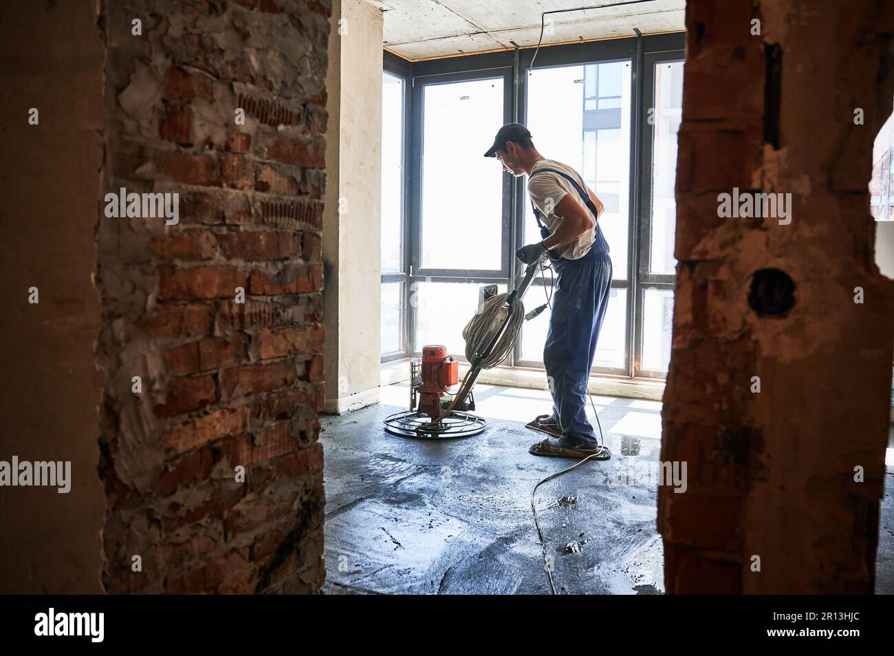 Male worker using troweling machine while screeding floor in apartment