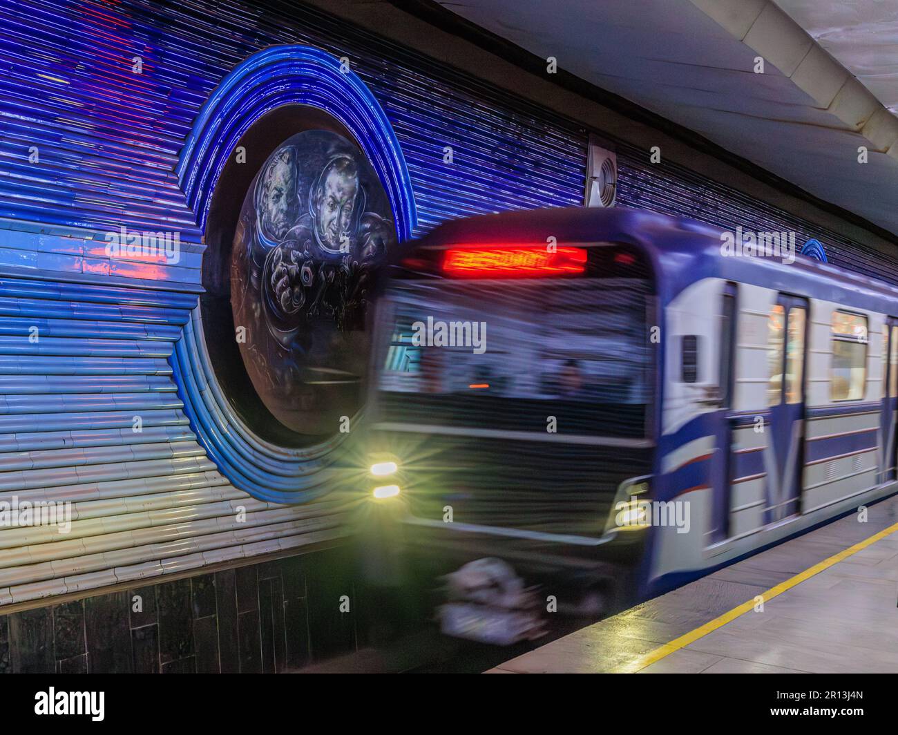 slow shutter photo of moving train arriving at cosmonaut metro station tashkent in front of panel celebrating conquerors of space Stock Photo