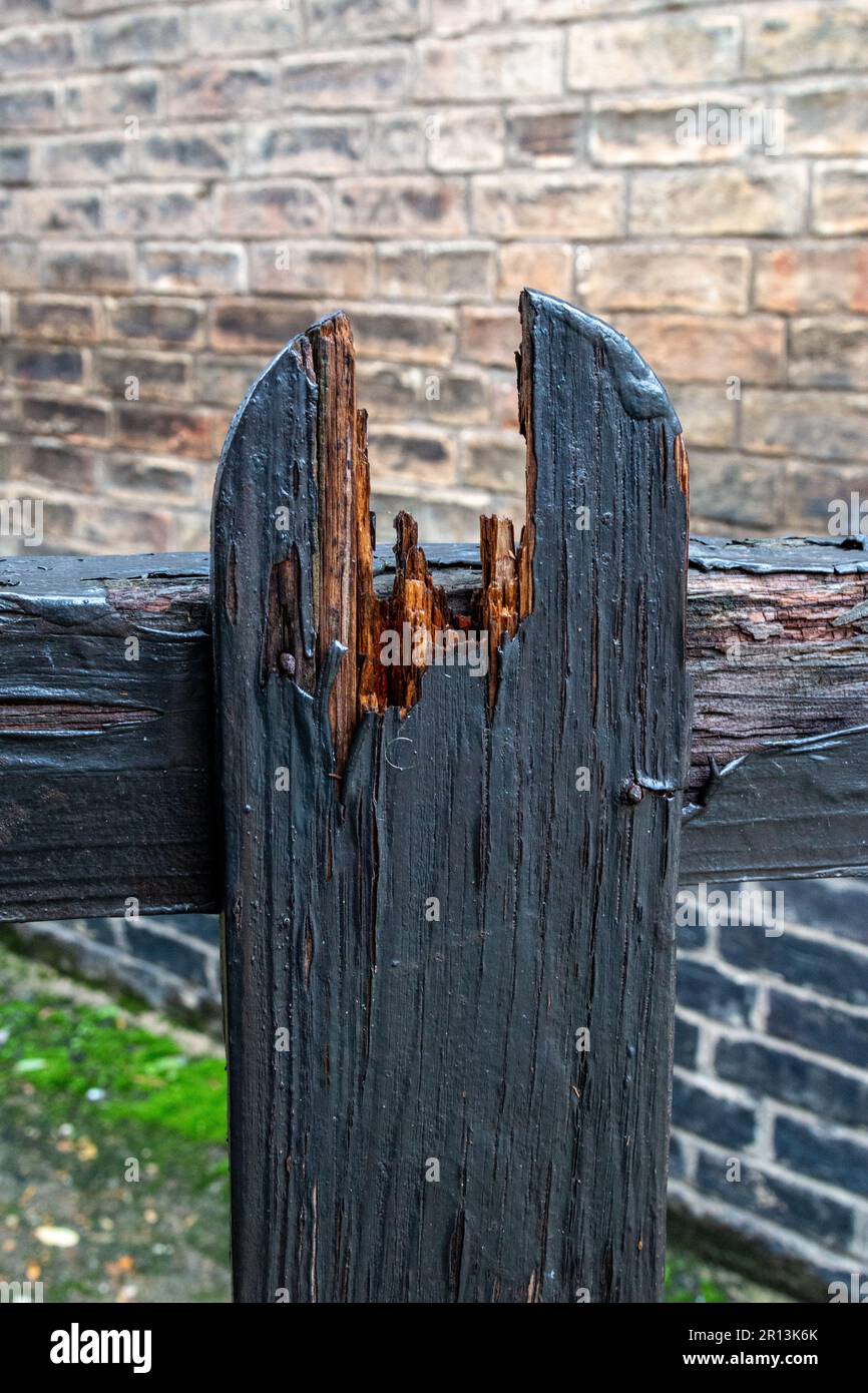 A broken gatepost shows the interior wood underneath the dark painted ...