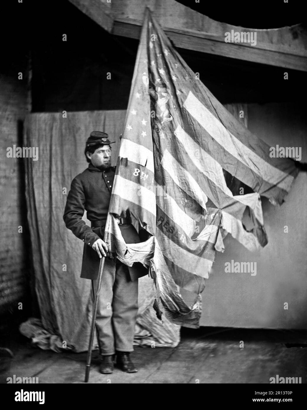 A battle scarred flag of the Pennsylvania Infantry held by a Union soldier.  Photograph from the Mathew Brady Collection. Photographer unknown. Stock Photo
