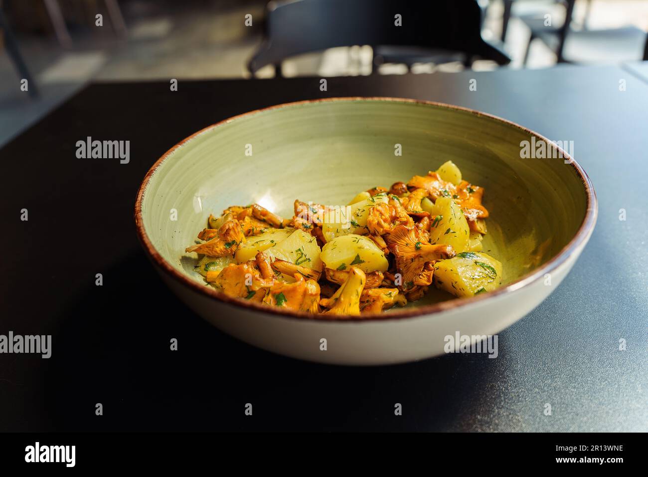 Fried chanterelles with boiled potatoes and green herbs, parsley and dill in a bowl for lunch. Stock Photo