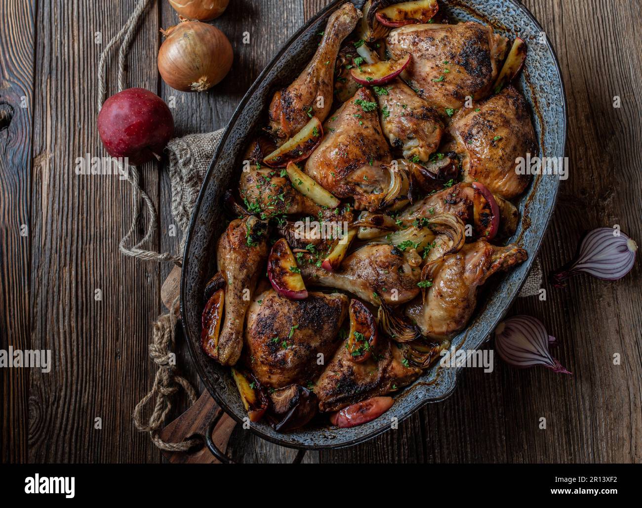 Meat dish for autumn, winter or thanksgiving with Oven roasted chicken Cooked with red apples and onions. Served in a rustic roasting pan isolated on Stock Photo