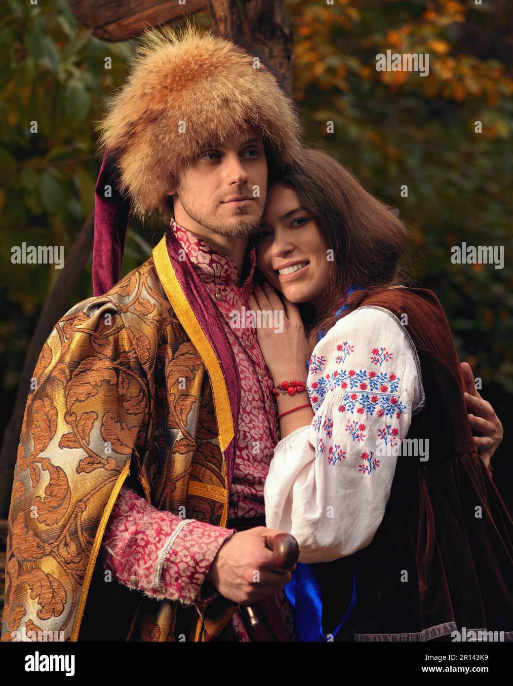 Young happy couple dressed traditional ukrainian clothing. Serious cossack man and smiling woman in embroidered costumes outdoors. Vintage outfit Stock Photo