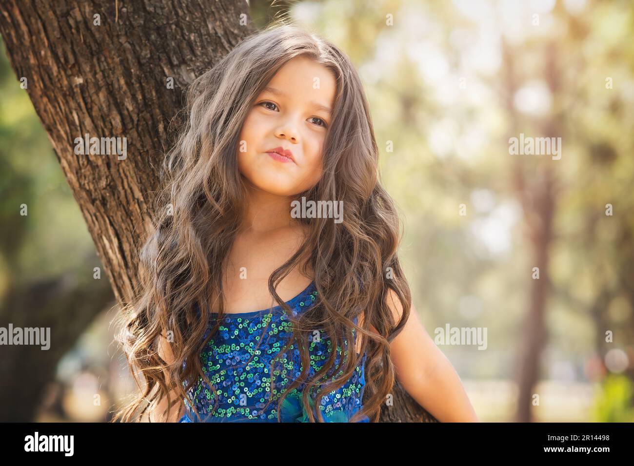 beautiful happy girl playing in the park with blue dress without shoes sitting on tree laughing screaming with happiness in family enjoying children's Stock Photo