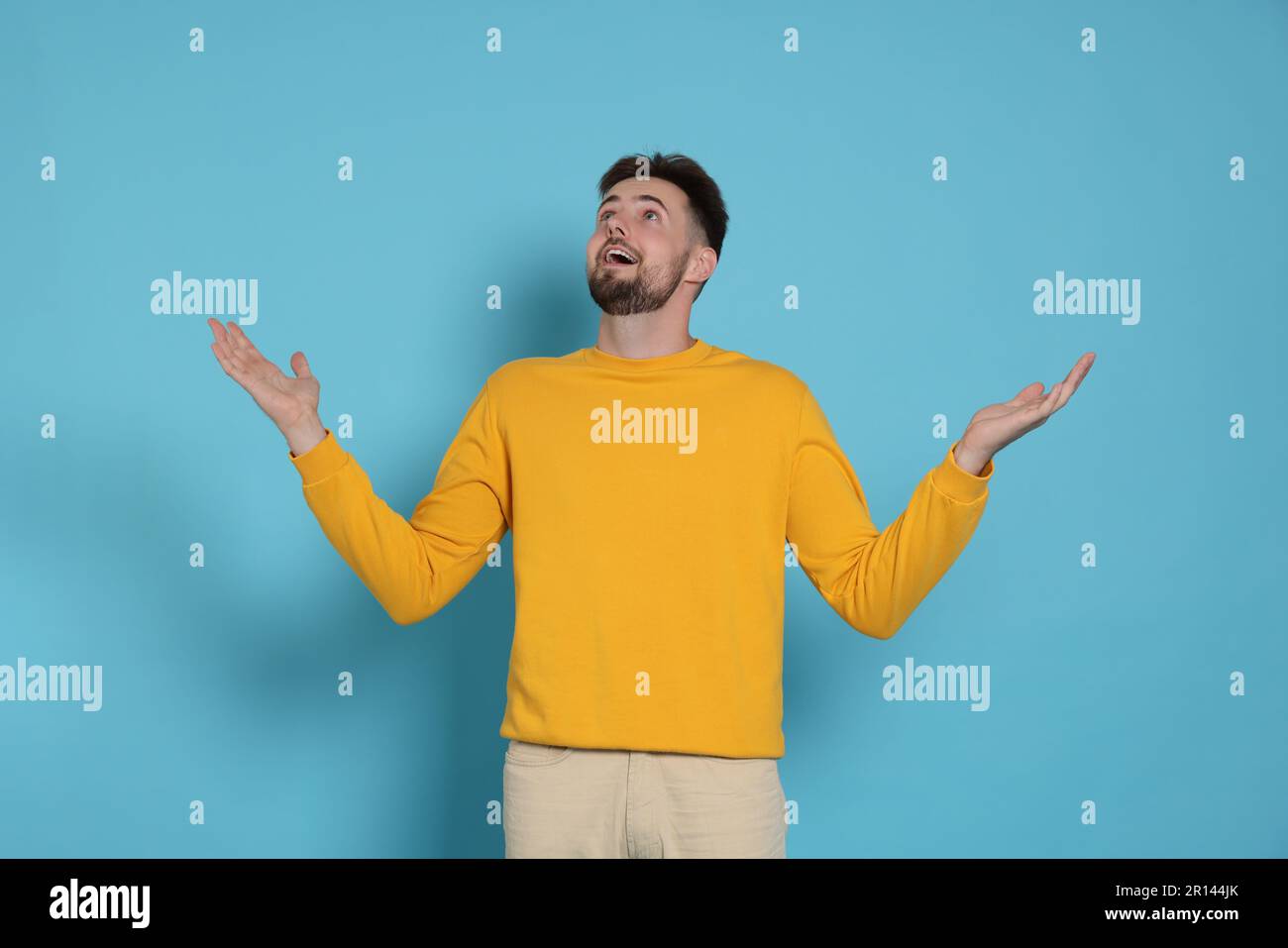 Surprised man in yellow sweatshirt on light blue background Stock Photo