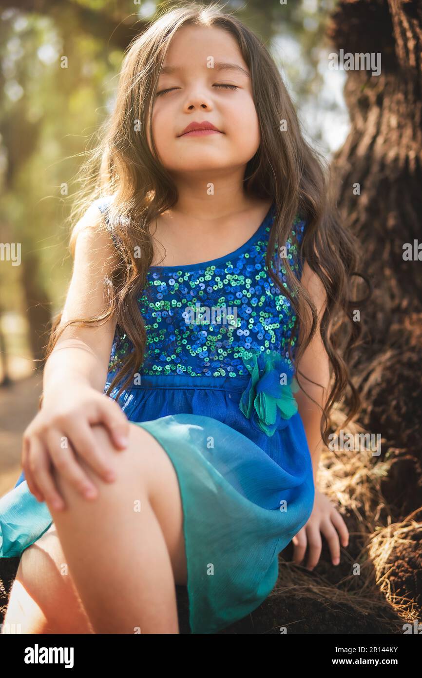 beautiful happy girl playing in the park with blue dress without shoes  sitting on tree laughing screaming with happiness in family enjoying  children's Stock Photo - Alamy, image size:866x1390
