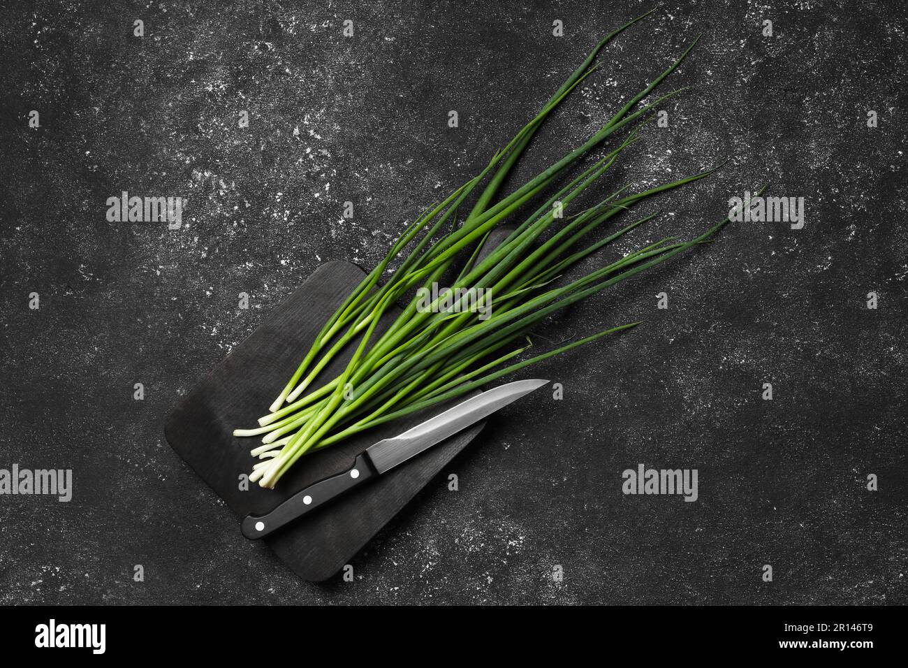 Fresh green onion and knife on black table, top view. Space for text ...