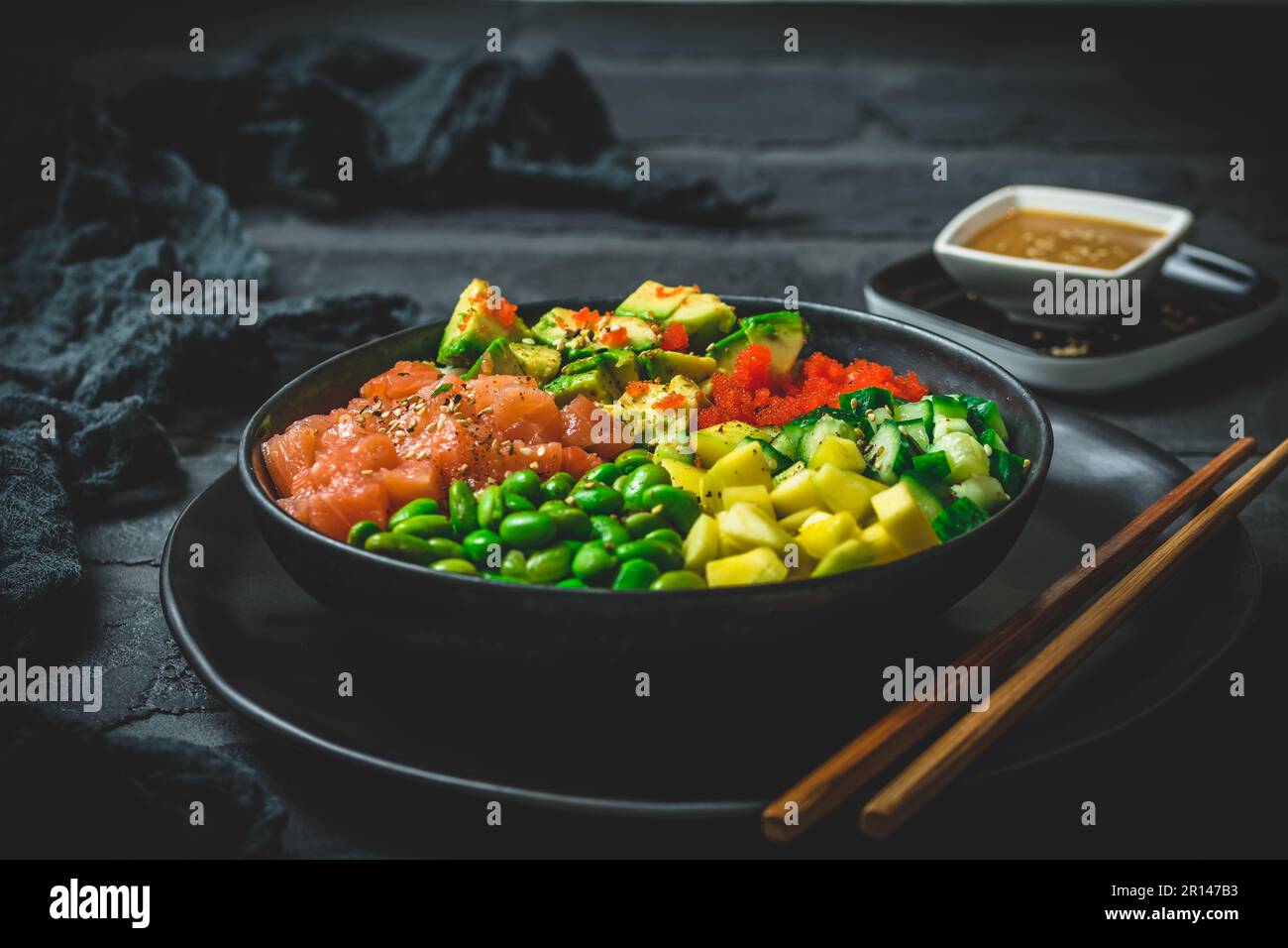 Japanese poke or buddha bowl with salmon, avocado, roe, mango, pies and cucumber in a black bowl on black background Stock Photo