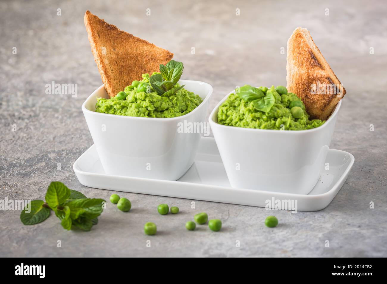 Two bowls of pea puree with basil, mint and roasted bread on rustic