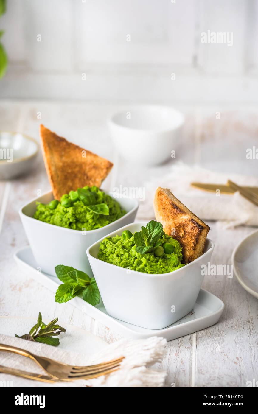 Two bowls of pea puree with basil, mint and roasted bread on rustic