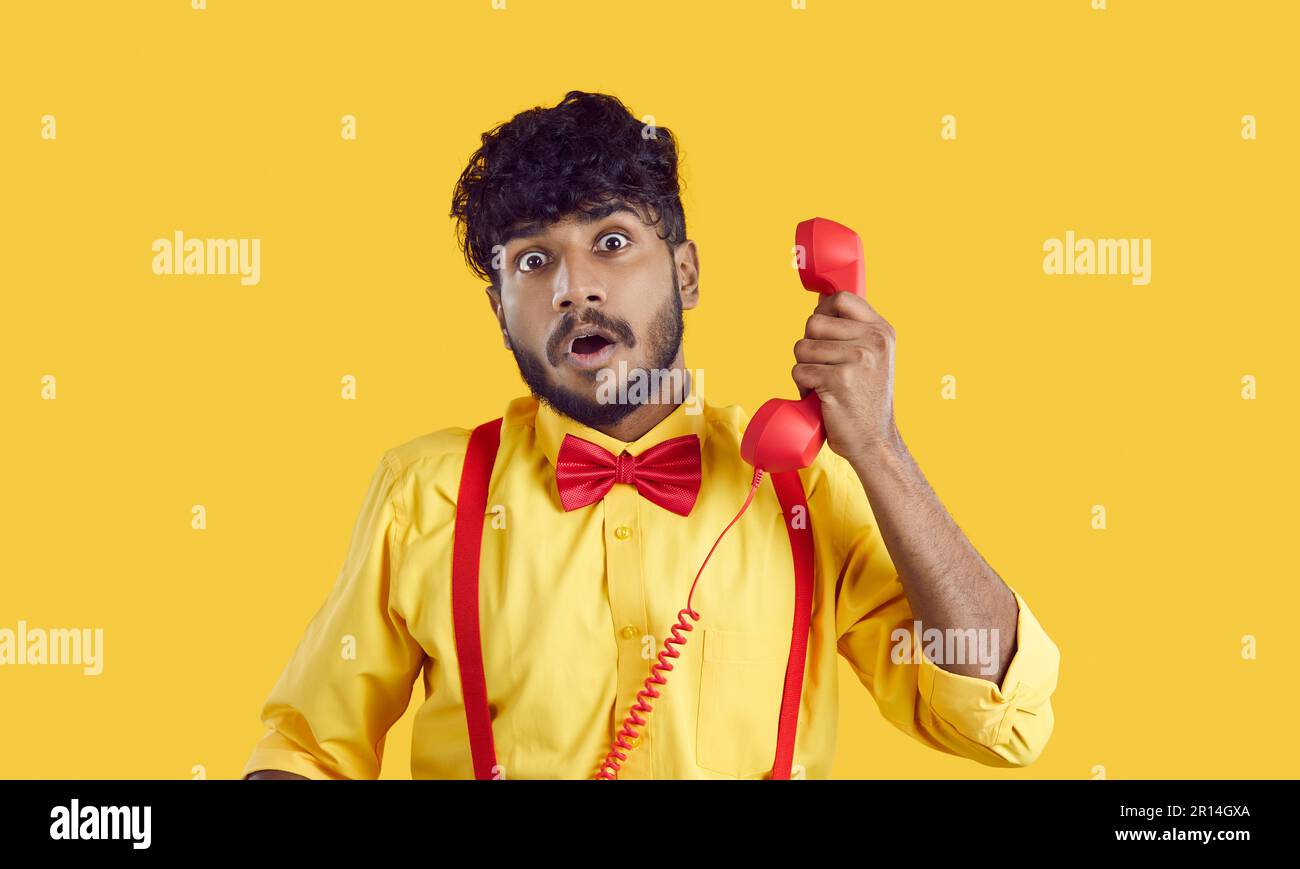 Funny Indian man talking on retro telephone with surprised, shocked, scared face expression Stock Photo