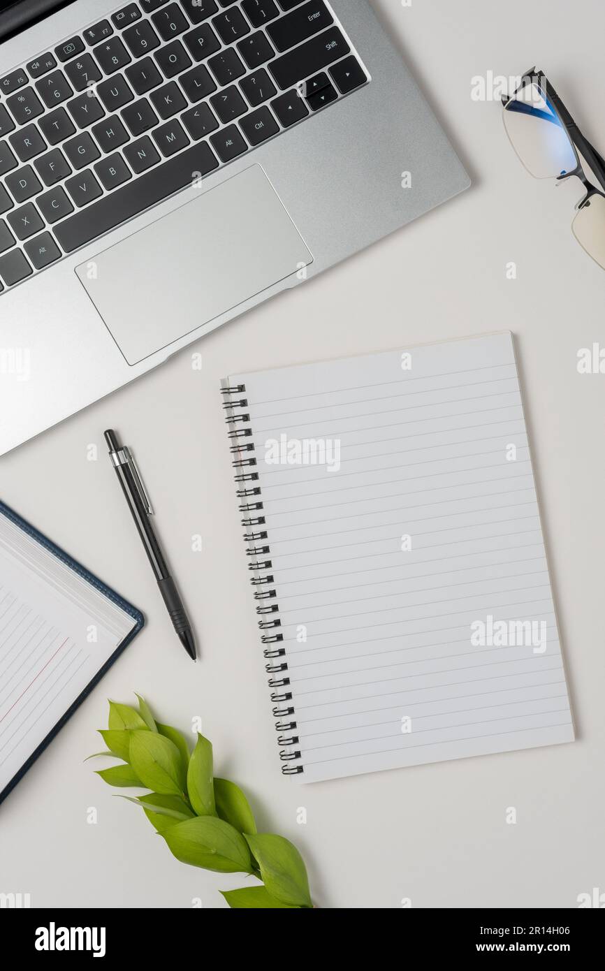 White office desk table with blank notebook, laptop and other office supplies. Top view with