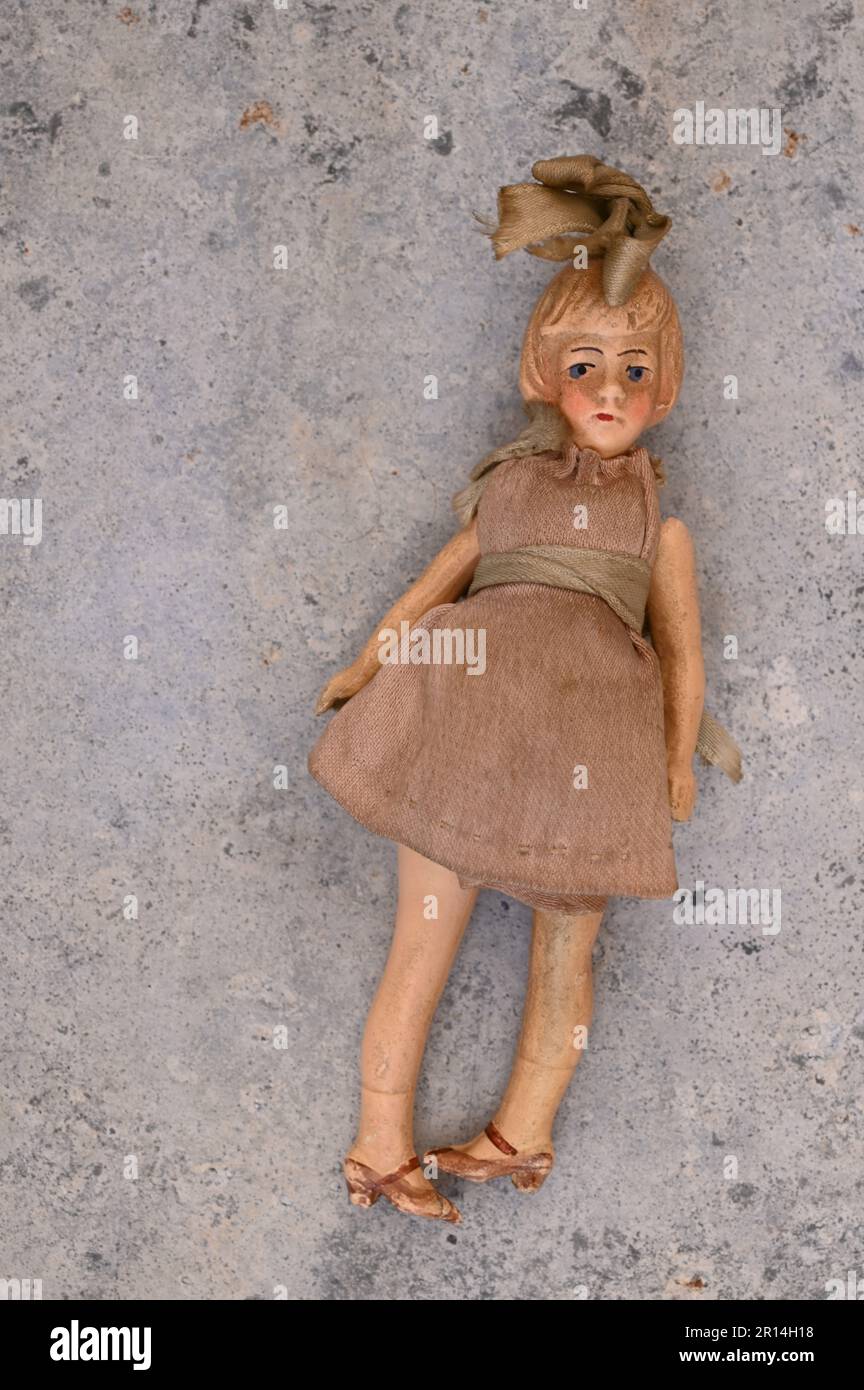 1910s girl doll with large bow in her hair and sad expression lying with feet turned inwards on marble Stock Photo