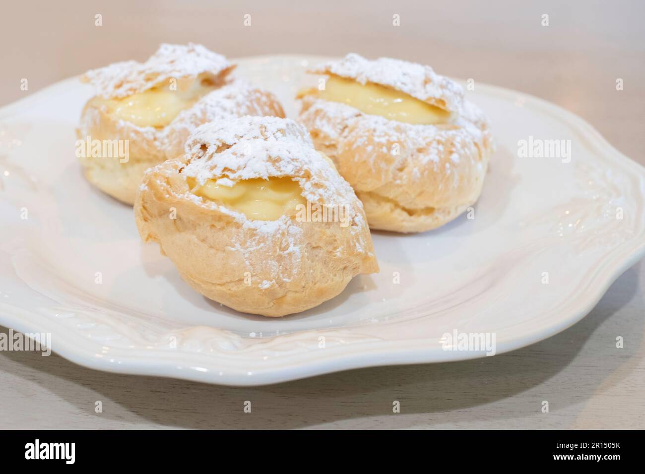 Three cream puffs, pate a choux, filled with vanilla cream pudding & sprinkled with powdered sugar. Sweet dessert. USA. Stock Photo