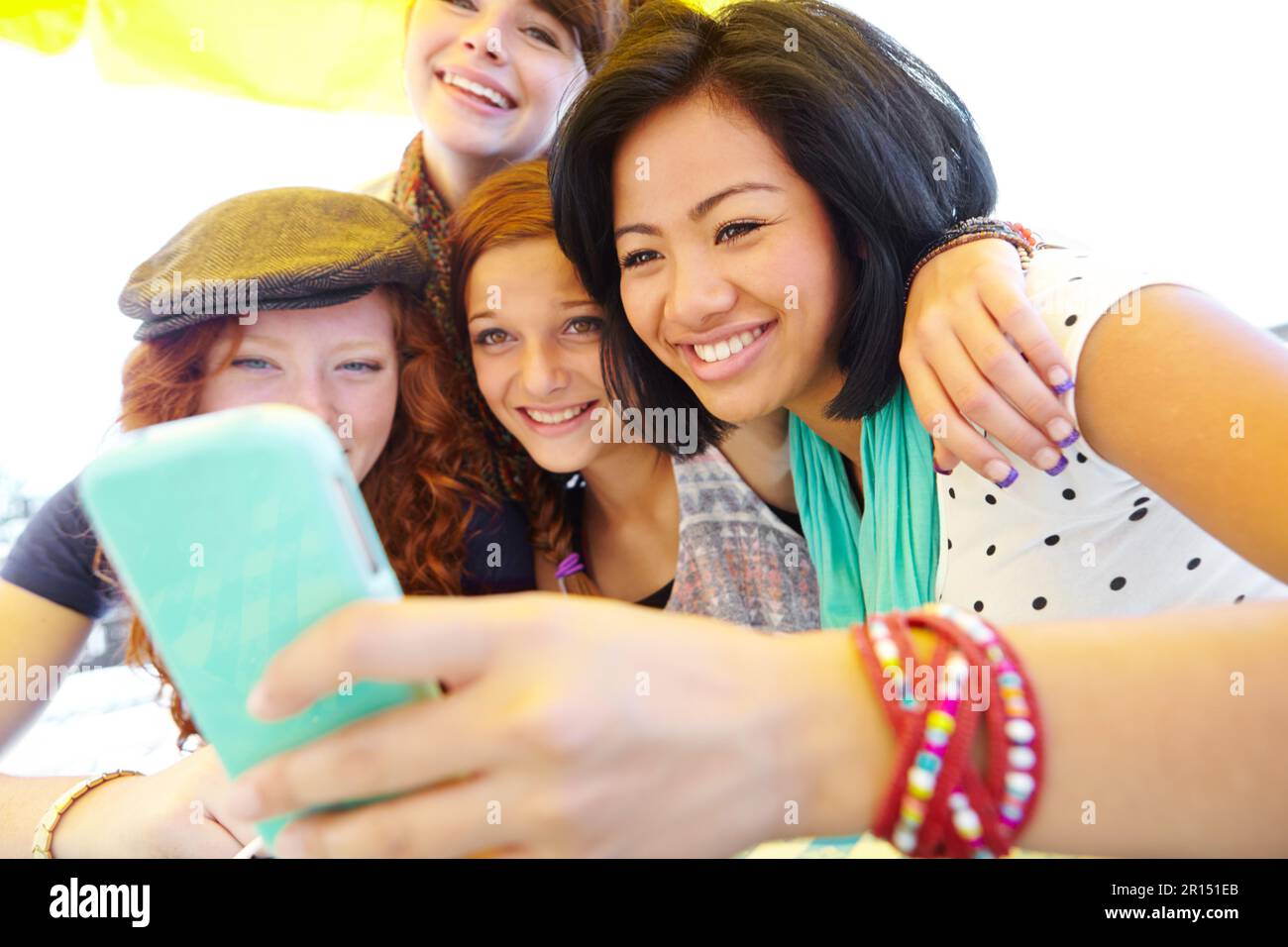 Lets update our profile pictures. A group of adolescent girls laughing as they look at something on a smartphone screen. Stock Photo